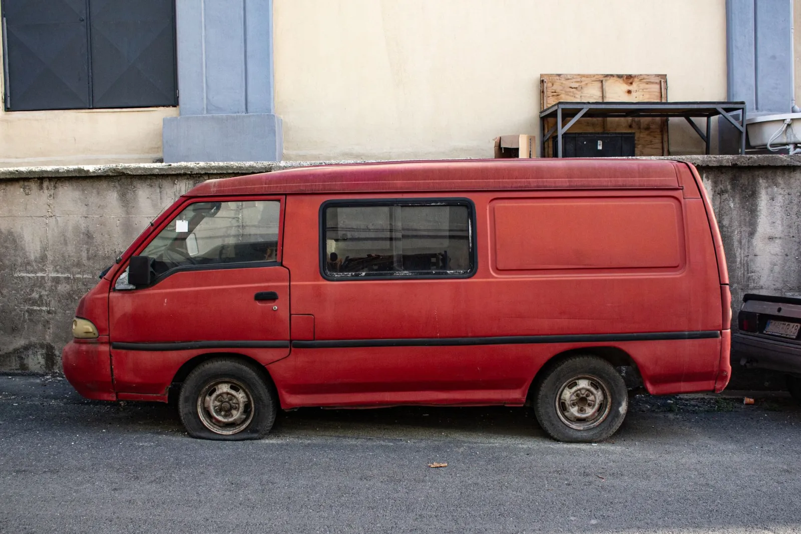 Abandoned red van with flat tire parked on urban pavement.